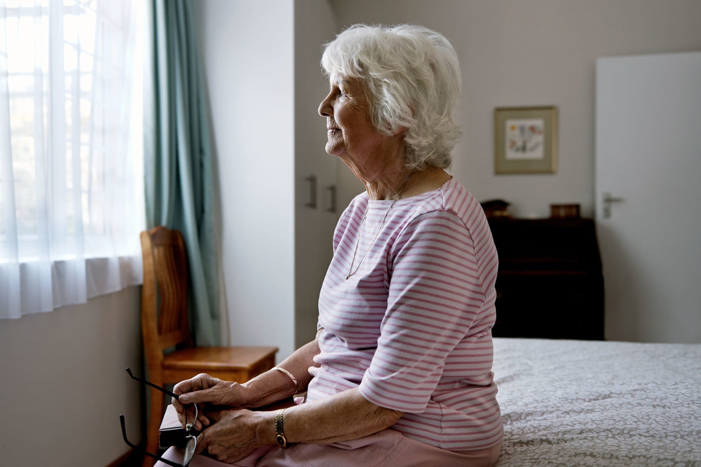 A solemn elderly woman sitting on her bed