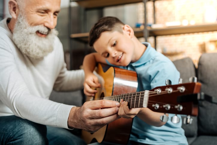 Smiling grandfather showing grandson how to play guitar