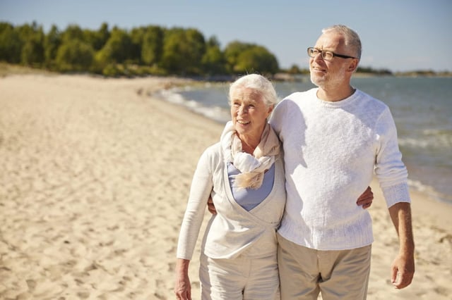 happy senior couple walking along summer beach