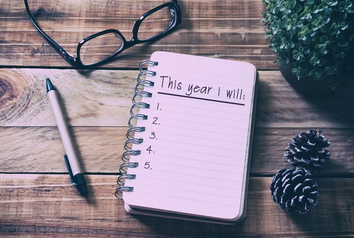 New Year Resolutions List on Notepad on Top of Wood Desk