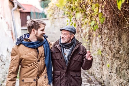 Old man walking outside alongside a young man and talking.